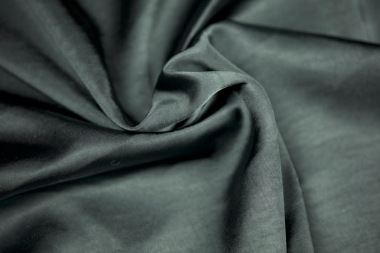 Nahaufnahme eines luxuriösen Satinstoffs in dunklem Schiefergrau mit elegantem Glanz und natürlichem Faltenwurf – ideal für stilvolle Nähprojekte