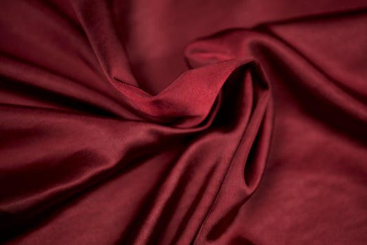Nahaufnahme eines luxuriösen Satinstoffs in kräftigem Bordeaux mit seidig glänzender Oberfläche und weichem Faltenwurf – ideal für Abendmode und Dekoration