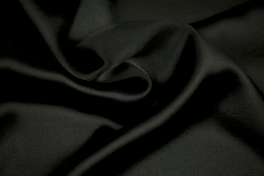 Nahaufnahme eines luxuriösen Satinstoffs in elegantem Schwarz mit weichem Faltenwurf und seidig glänzender Oberfläche.